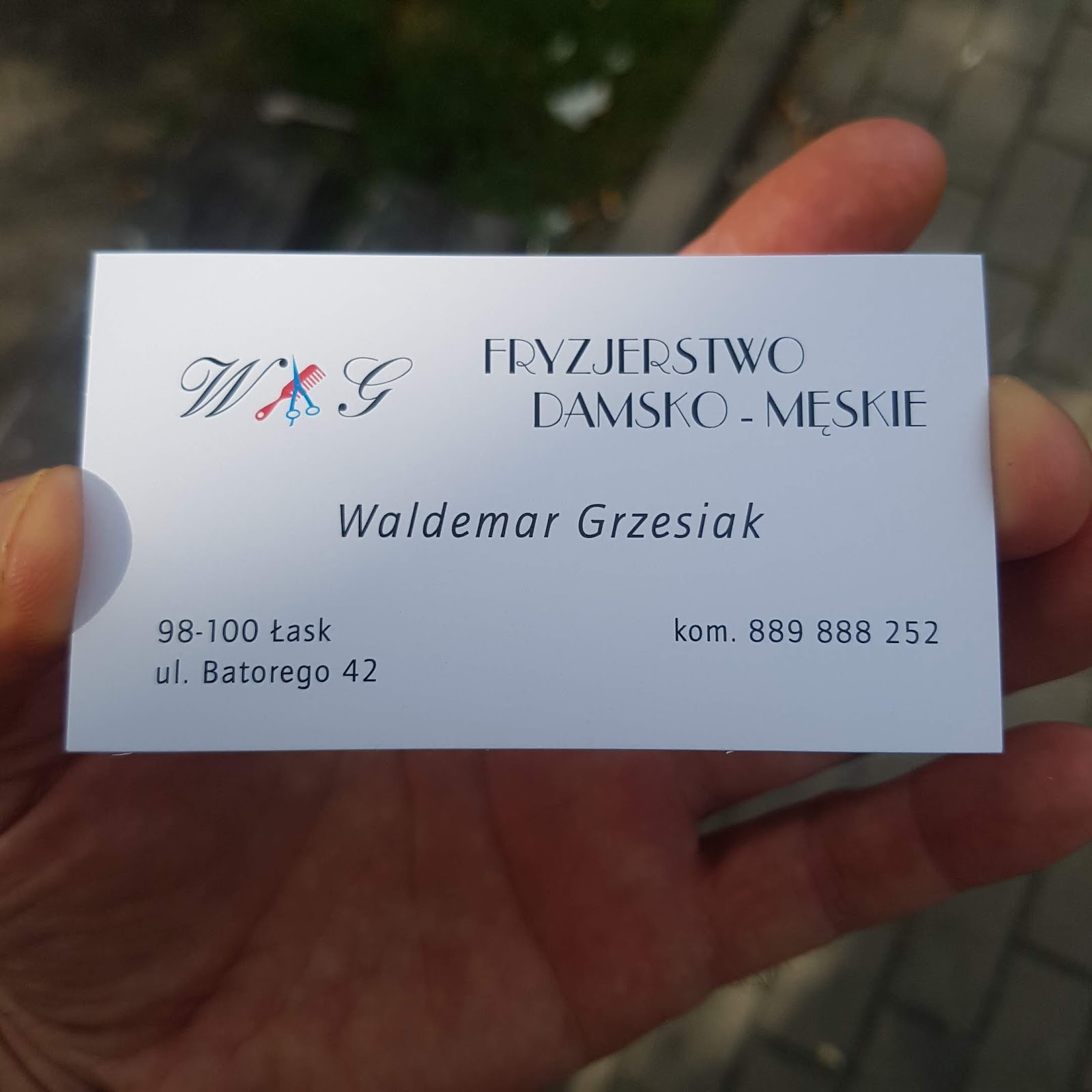 Wizytówka zakładu Waldemara Grzesiaka z monogramem W.G., nożyczkami i grzebieniem w czerwono-niebieskich akcentach